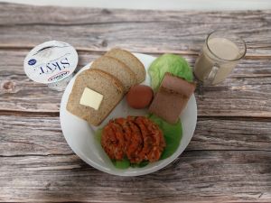 Zdjęcie przedstawia Dietę z ograniczeniem łatwoprzyswajalnych węglowodan&oacute;w: Masło extra 82% Pasztet drobiowy z kurnej p&oacute;łki Pasta warzywna Kawa zbożowa z mlekiem Chleb Graham Jogurt typu islandzkiego naturalny Skyr Sałata zielona Jajko gotowane